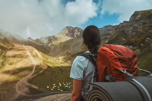 Hiker with red backpack is standing on top of a mountain and enjoying camping valley view stock photo