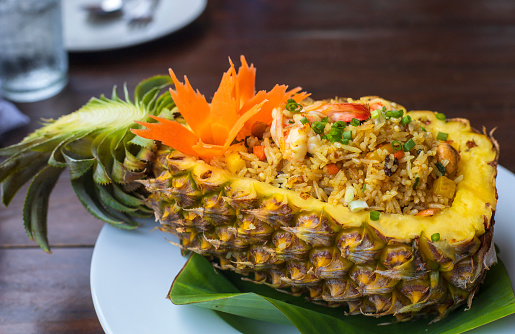 Thai royal pineapple fried rice. Fried rice with shrimps served in a pineapple on wood table.