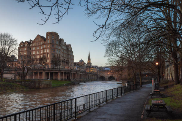 vue de la rivière avon de la promenade au bord de la rivière avec le pont pulteney et le fond historique de bâtiment et le premier plan sec d'arbre pendant le coucher du soleil à bath, r-u - uk tree city bridge photos et images de collection