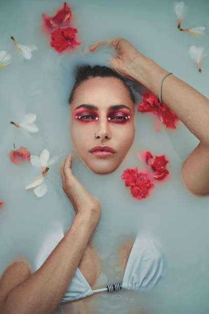 Fashion portrait of beautiful woman with red and white flowers in a bath with milk stock photo