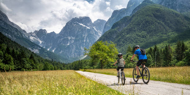 Father and son on a cycling trip to the mountains Scenic photo of a father and his son on mountain bike riding on a country road towards the mountains of the European Alps. slovenia stock pictures, royalty-free photos & images
