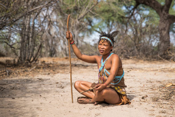 San woman in Makgadikgadi, Botswana, Africa Makgadikgadi, Botswana - October 24, 2018:  Woman of the San tribe is sitting on the sandy ground, she is dressed in traditional clothing of the San tribe. The San belong to the bushman people. bushmen stock pictures, royalty-free photos & images