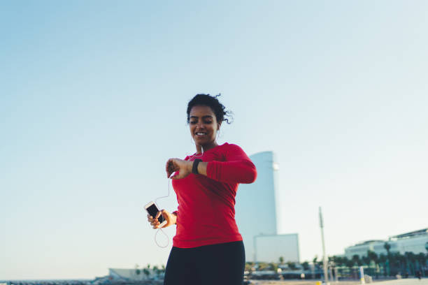 Sportswoman jogging in Barcelona Woman checking pulse on smart watch while jogging fitness tracker photos stock pictures, royalty-free photos & images