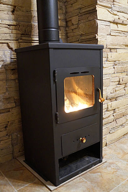 istock Metal stove fireplace with fire behind glass in the interior, side view 1200751133