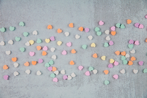 scattered conversation heart pastel colored candies for Valentine's Day on Gray Grey Cement background and copy space for text and writing