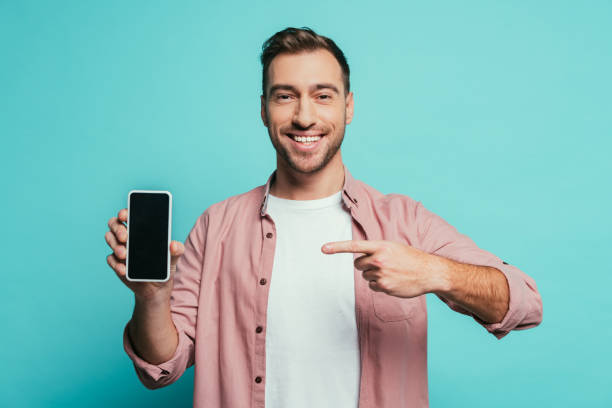 istock smiling man pointing at smartphone with blank screen, isolated on blue 1200755685