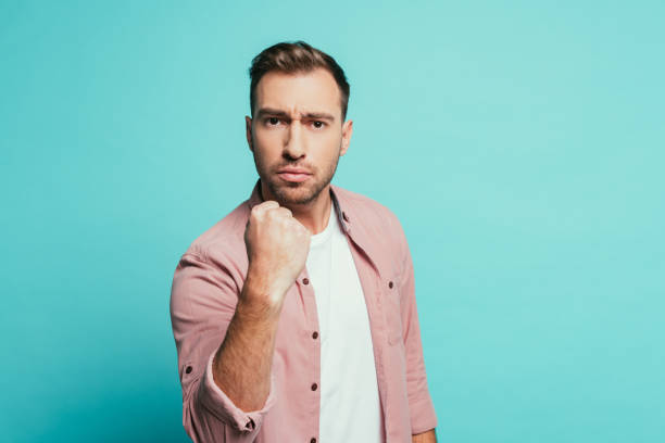 istock angry handsome man showing fist, isolated on blue 1200755694