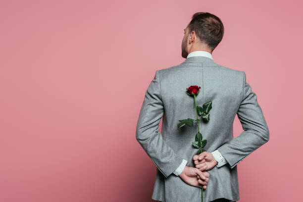 back view of man in suit holding red rose, isolated on pink back view of man in suit holding red rose, isolated on pink hands behind back stock pictures, royalty-free photos & images