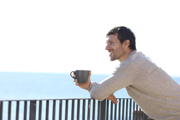 istock Happy man holding cup contemplating views from a balcony 1200762419