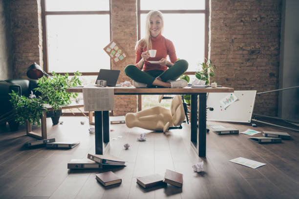 Full body photo of happy trader woman sit on table crossed legs feel carefree careless rest relax hold white coffee cup in messy office loft Full body photo of happy trader woman sit on table crossed legs feel carefree, careless rest relax hold white coffee cup in messy office loft chaos stock pictures, royalty-free photos & images
