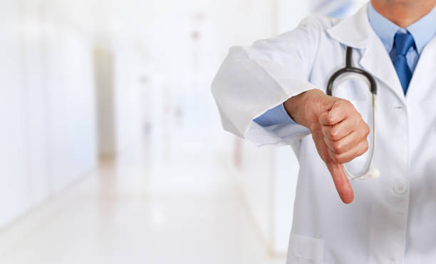 doctor hand gesturing thumbs down Closeup of a male doctor hand gesturing thumbs down as symbol of disapproval at hospital thumb down stock pictures, royalty-free photos & images