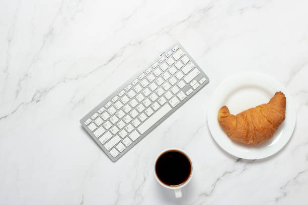 istock Cup of coffee, a croissant and a keyboard on a marble table. Concept breakfast at work, freelance, french breakfast, work at home. Flat lay, top view 1200774223