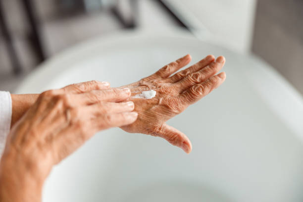 elderly lady applying moisturizing cream on hand - moisturizer cosmetics merchandise human hand imagens e fotografias de stock