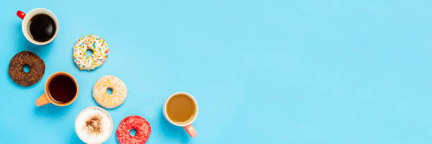 istock Tasty donuts and cups with hot drinks, coffee, cappuccino, tea on a blue background. Concept of sweets, bakery, pastries, coffee shop, meeting, friends, friendly team. Banner. Flat lay, top view 1200778123