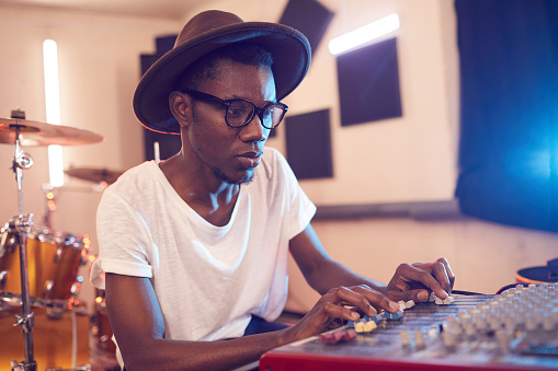 Portrait of young African-American man writing music in recording studio using sound equalizing mixer, copy space