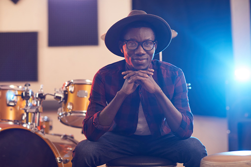Portrait of contemporary African man looking at camera and smiling cheerfully while posing in music recording studio
