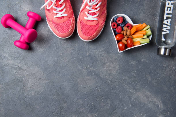 健身理念，粉紅色運動鞋，啞鈴，一瓶水和心形板與蔬菜和漿果在灰色背景，頂視圖，健康的生活方式 - 運動訓練 圖片 個照片及圖片檔