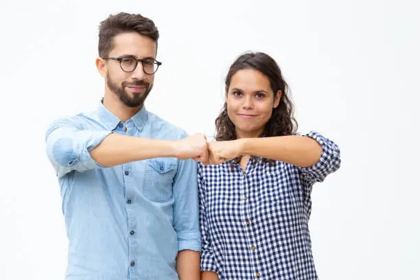 Content young couple touching fists. Front view of happy young man and woman showing fist bump gesture and smiling at camera on white background. Togetherness concept