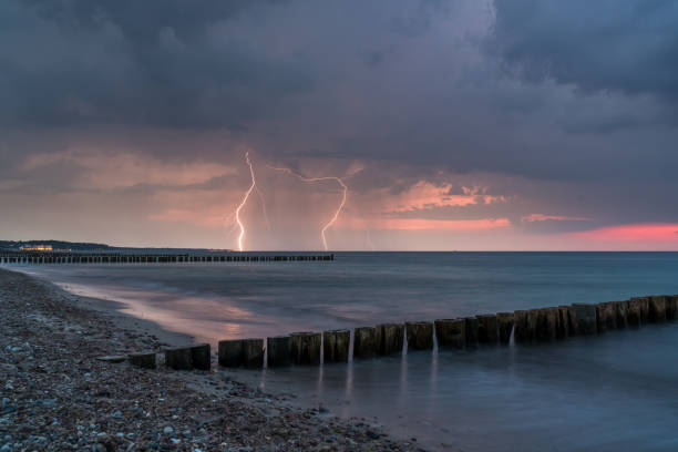 krajobraz strzał burzy z błyskami uderzające w oceanie uchwycone na plaży tuż po zachodzie słońca z groynes na pierwszym planie - sunset beach flash zdjęcia i obrazy z banku zdjęć