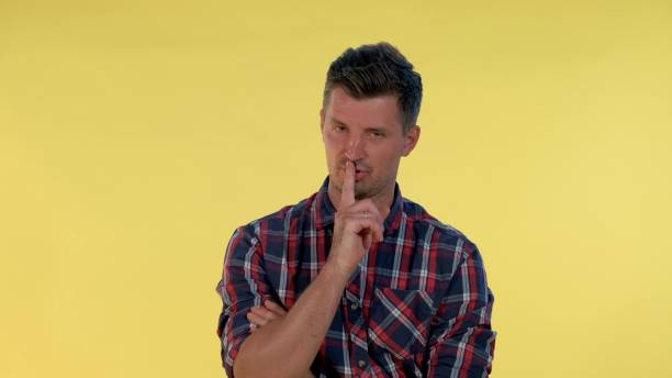 istock Close up of young man making a hush gesture on yellow background 1200781641
