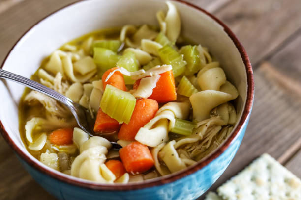 나무 테이블에 야채와 크래커를 곁들인 수제 유기농 치킨 누들 수프의 파란색 그릇 - soup carrot celery chicken 뉴스 사진 이미지