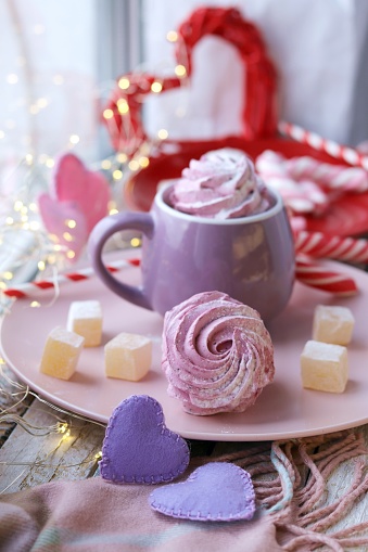 Cup of coffee with meringues and marshmallows, Turkish delight on a plate, hearts, illumination, against the background of a window, homeliness, Valentine's day