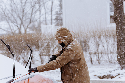 Man cleaning a car covered by snow
