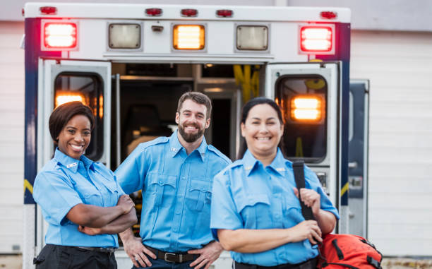 Paramedics standing at the rear doors of an ambulance A multi-ethnic group of three paramedics standing at the rear of an ambulance, in front of the open doors . The focus is on the young man with his hands on his hips and the young African-American woman with her arms folded. Their coworker is a mature Hispanic woman, carrying a medical trauma bag. They are smiling at the camera. emt stock pictures, royalty-free photos & images