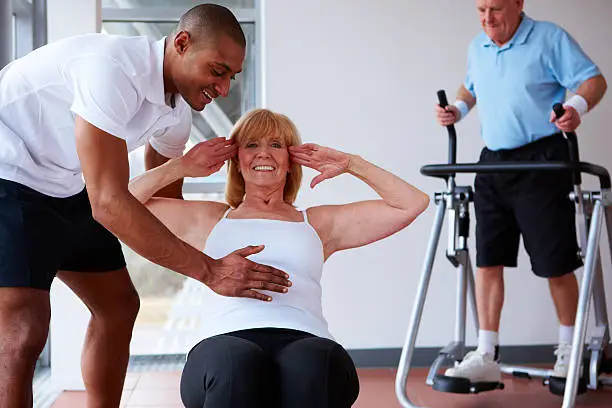 Personal trainer helps a senior woman maintain form while performing sit-ups.