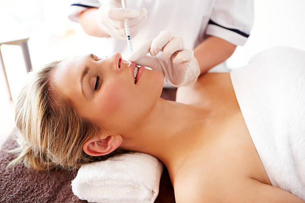 Woman Receiving a Beauty Treatment Injection Young woman lies on her back while getting an injection to enlarge her lips. fish lips stock pictures, royalty-free photos & images