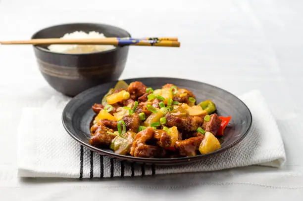 Sweet and sour pork with rice bowl. Deep fried meat is added to stir fried pineapple, onions, peppers and sauce. Sweet and sour dishes are common in asian cuisine, especially American Chinese food.