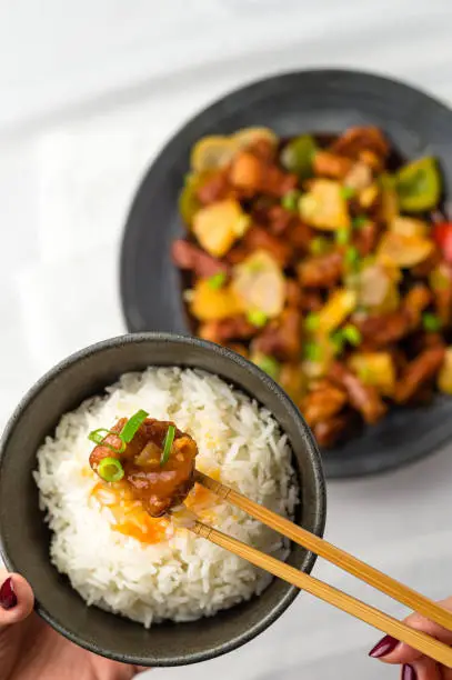 Sweet and sour pork on chopsticks. Deep fried meat is added to stir fried pineapple, onions, peppers and sauce. Sweet and sour dishes are common in asian cuisine, especially American Chinese food.