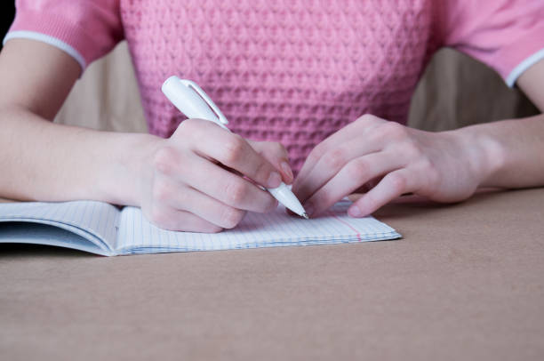 istock A girl in a pink blouse writes in a notebook with a pen 1200827648