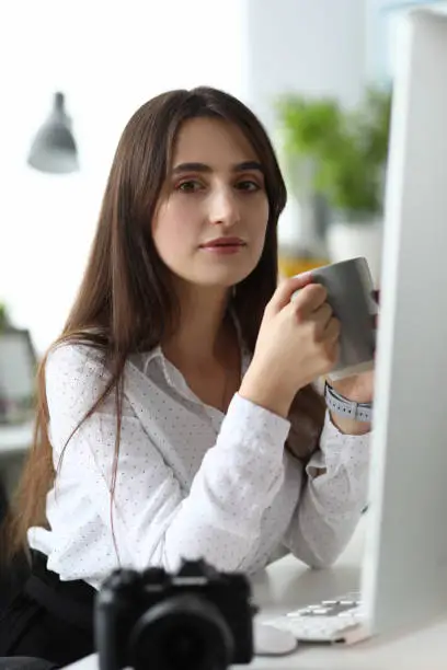 Portrait of beautiful businesslady drinking coffee and wondering about future projects. Pretty woman wearing casual white blouse. Business and art design concept. Blurred background