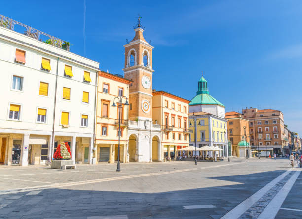 Piazza Tre Martiri Three Martyrs square with traditional buildings with clock and bell tower in old historical touristic city centre Rimini with blue sky background, Emilia-Romagna, Italy