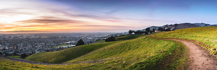 Sunset view of hiking trail on the verdant hills of East San Francisco Bay Area; the city of Hayward and the bay visible in the valley; California