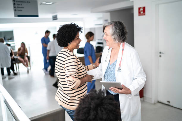 female senior doctor welcoming / greeting mother and daughter at hospital - doctor patient greeting talking imagens e fotografias de stock