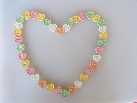 Heart-shaped candies form a Valentine, white background (conversation hearts), copy space