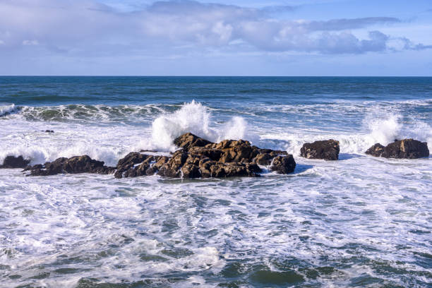 Large ocean waves crashing on rocky California pacific rocks, with clouds in the background.\n\nTaken at Pescadero State Beach, California, USA