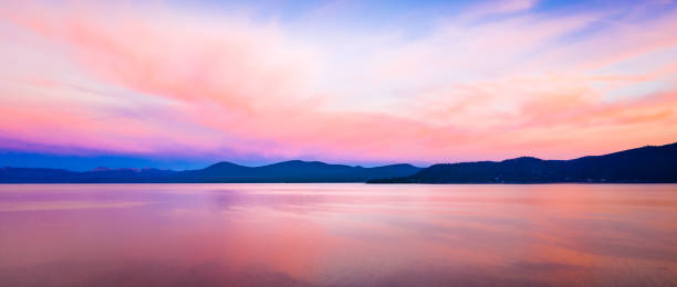 istock Panoramic background with brilliant colorful sky reflecting off the water at sunset with mountains at the horizon 1200842463