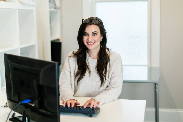 istock smiling Brunette woman working on a computer in a small mostly white modern home office 1200844746