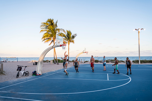 Fort Lauderdale, Florida, USA - January 15, 2020: A group of men play a game of basketball at sunset on the beautiful basketball court at Fort Lauderdale Beach Park.