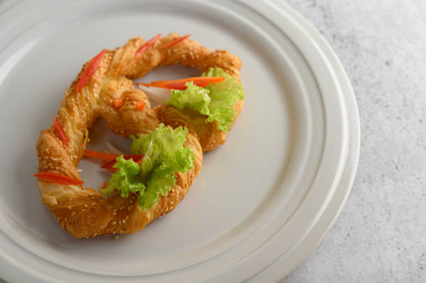 Freshly baked soft pretzel with generous sprinkling of coarse salt and sesame on white dish, decorate with lettuce and carrot beautifully, copy space