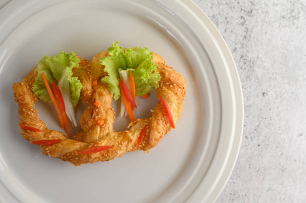 Freshly baked soft pretzel with generous sprinkling of coarse salt and sesame on white dish, decorate with lettuce and carrot beautifully, copy space