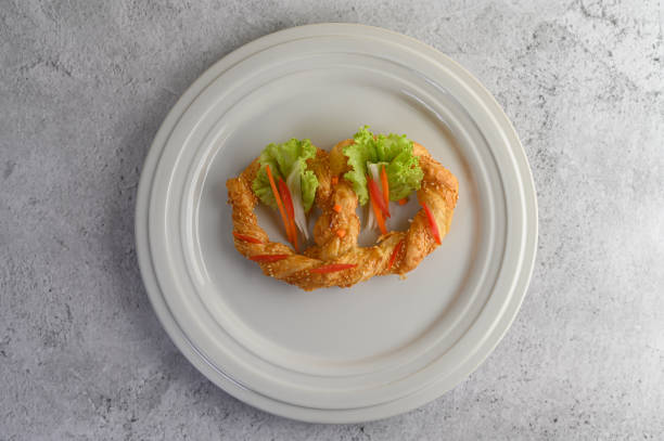 Freshly baked soft pretzel with generous sprinkling of coarse salt and sesame on white dish, decorate with lettuce and carrot beautifully, copy space