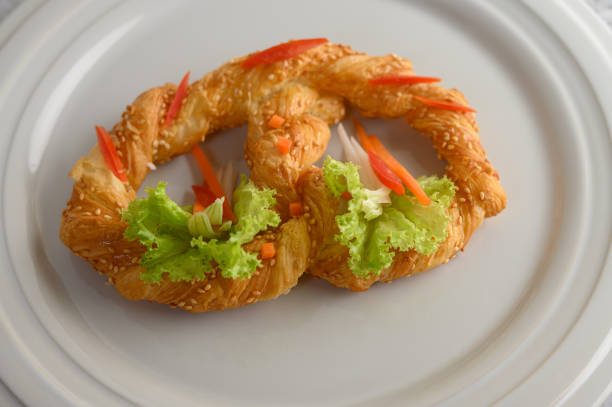 Freshly baked soft pretzel with generous sprinkling of coarse salt and sesame on white dish, decorate with lettuce and carrot beautifully, copy space