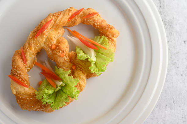 Top view Freshly baked soft pretzel with generous sprinkling of coarse salt and sesame on white dish, decorate with lettuce and carrot beautifully, copy space