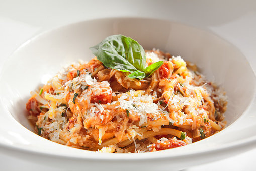 Classical italian spaghetti with tomatoes, tomato sauce, basil, milk mozzarella and parmesan cheese on white restaurant plate isolated. Macro shot of bucatini pasta, pici or stringozzi noodles