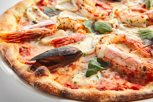 Italian seafood pizza with squid rings, mussels and shrimps on white restaurant plate isolated. Pizza ai frutti di mare topped with tomato sauce, basil and mozzarella closeup
