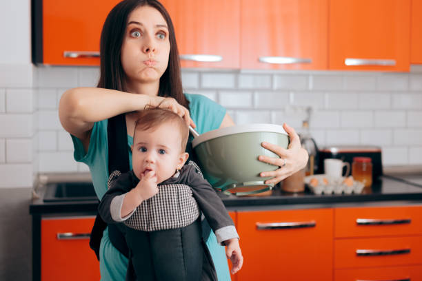 mamma impegnata che cucina tenendo il bambino nel sistema di babywearing carrier - mother emotional stress exhaustion cooking foto e immagini stock